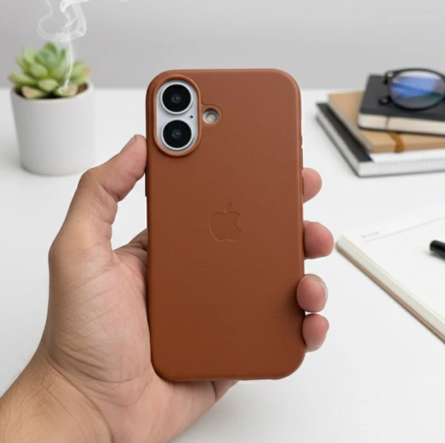 Hand holding a brown leather MagSafe case for iPhone.