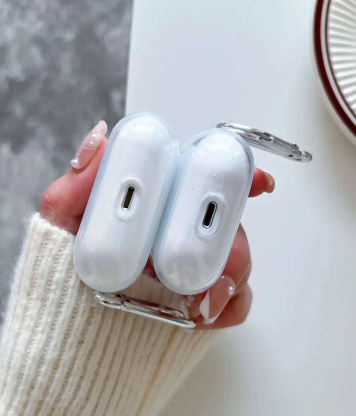 Transparent airpods case with carabiner held by a hand.