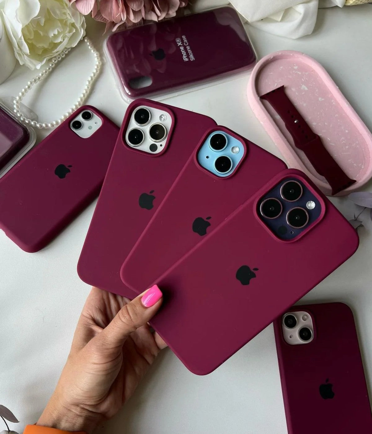 Plum iPhone silicone cases held by a hand on a white surface.