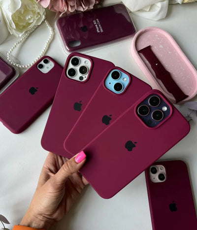 Plum iPhone silicone cases held by a hand on a white surface.