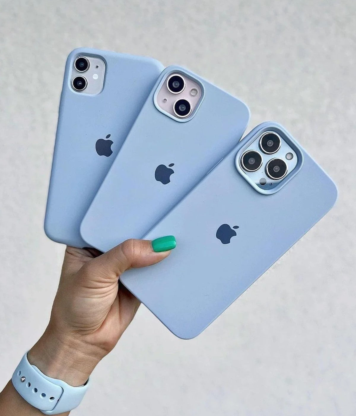 Sky blue iPhone silicone cases held by a hand on a white surface.